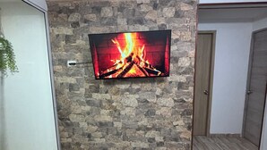 A living room with a stone wall, a flat-screen TV, a teal ottoman, and a door. - BAM - Lodging (Santa Marta)