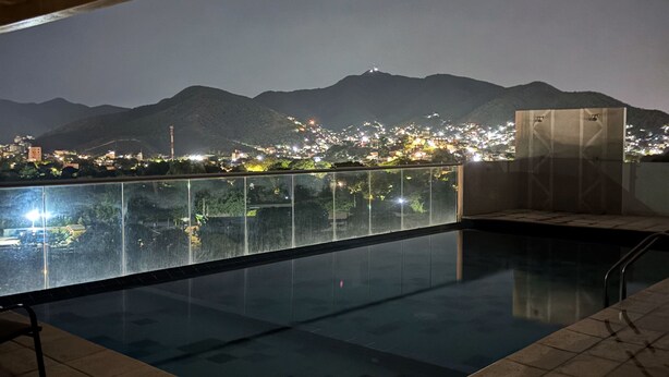 An indoor swimming pool with a view of a cityscape and mountains at night. - BAM - Lodging (Santa Marta)