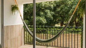 A modern living room with a large sliding glass door leading to a balcony with a hammock and a view of greenery. - BAM - Lodging (Santa Marta)