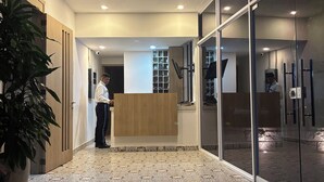A reception area with a wooden counter, patterned floor tiles, and a large potted plant. - BAM - Lodging (Santa Marta)