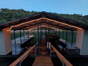A covered dock with a boat, wooden railings, and a view of the water.