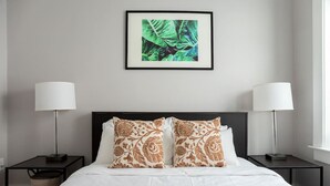A hotel room with a bed, two nightstands, two lamps, and a framed artwork on the wall.