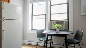 A kitchen with a white refrigerator, a window with blinds, a radiator, and two chairs around a small table with a potted plant. - Airy 1BR Walkable to Everywhere in Boston | W+D (Boston)