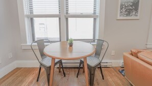 A room with a round wooden table, two grey chairs, a small potted plant, and a sofa. - Bay Village Charming 1 Bedroom Apartment (Boston)