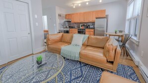 A modern living room with a leather sofa, a coffee table, and a kitchen in the background. - Bay Village Charming 1 Bedroom Apartment (Boston)