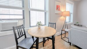 Une pièce comprenant une table ronde en bois, quatre chaises, un canapé gris et un lampadaire.