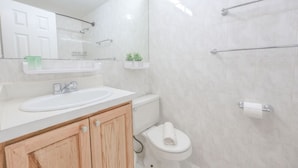 Ein modernes Badezimmer mit einem weißen Waschbecken, Holzschränken, einer Toilette und einer Duschkabine aus Glas.