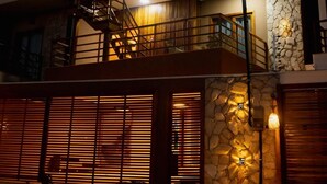 A two-story building with a stone facade, a balcony with a wooden railing, and a covered outdoor area with lights. - House in Prea  (Caiçara)