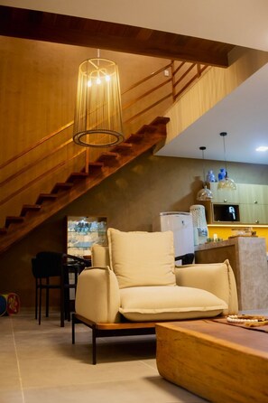 Ein modernes Wohnzimmer mit Treppe, einer Couch, einem Couchtisch und einer Küchenzeile inklusive Kühlschrank und Schränken.