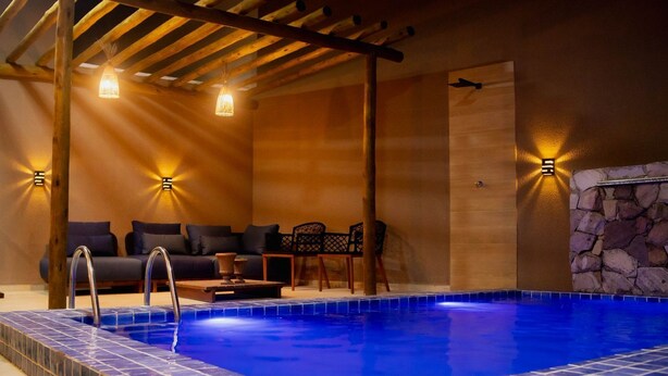 A pool area with a wooden ceiling, a stone wall, and a seating area with a sofa and chairs. - House in Prea  (Caiçara)