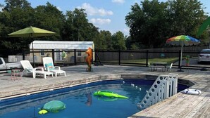 Una terraza de madera con piscina, juguetes inflables y sombrillas.