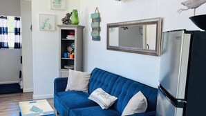 Una sala moderna con un sofá azul, una pequeña mesita auxiliar, un refrigerador y un aire acondicionado instalado en la pared.