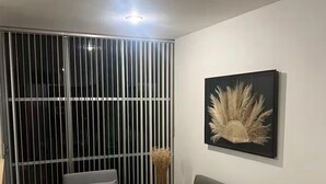 Un soggiorno moderno con un divano grigio, un tavolo bianco e un separé in vetro con persiane verticali.