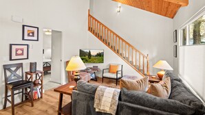 Uma sala de estar com escada de madeira, um sofá, uma mesa de centro e um quadro na parede.
