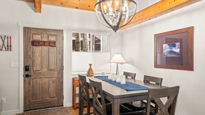 Uma sala de jantar com uma mesa de madeira, cadeiras, um candelabro, um vaso e um quadro na parede.