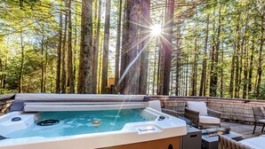 Ein Whirlpool, umgeben von hohen Bäumen, mit einer Holzterrasse und Gartenmöbeln.