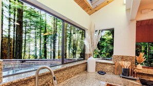 Eine Küche mit Granit Arbeitsplatten, einer Edelstahl-Spüle und einem großen Fenster mit Blick auf einen Wald.