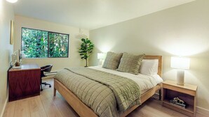 Ein Schlafzimmer mit einem Bett, Nachttischlampen, einem Schreibtisch und einem Fenster mit Blick auf Grünflächen.