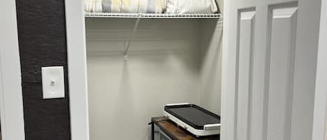 A compact room with a white door, a small shelf with a microwave, and a bed with a checkered blanket.