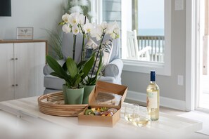 A dining table with a wicker tray, a box of food, a bottle of wine, and potted plants. - Do Knot Disturb Oceanfront Private Pool Renovated Sleeps 14 (Emerald Isle)