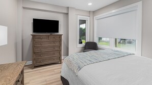 Une chambre à coucher comprenant un lit, une commode, un téléviseur et une fenêtre donnant sur l’extérieur.