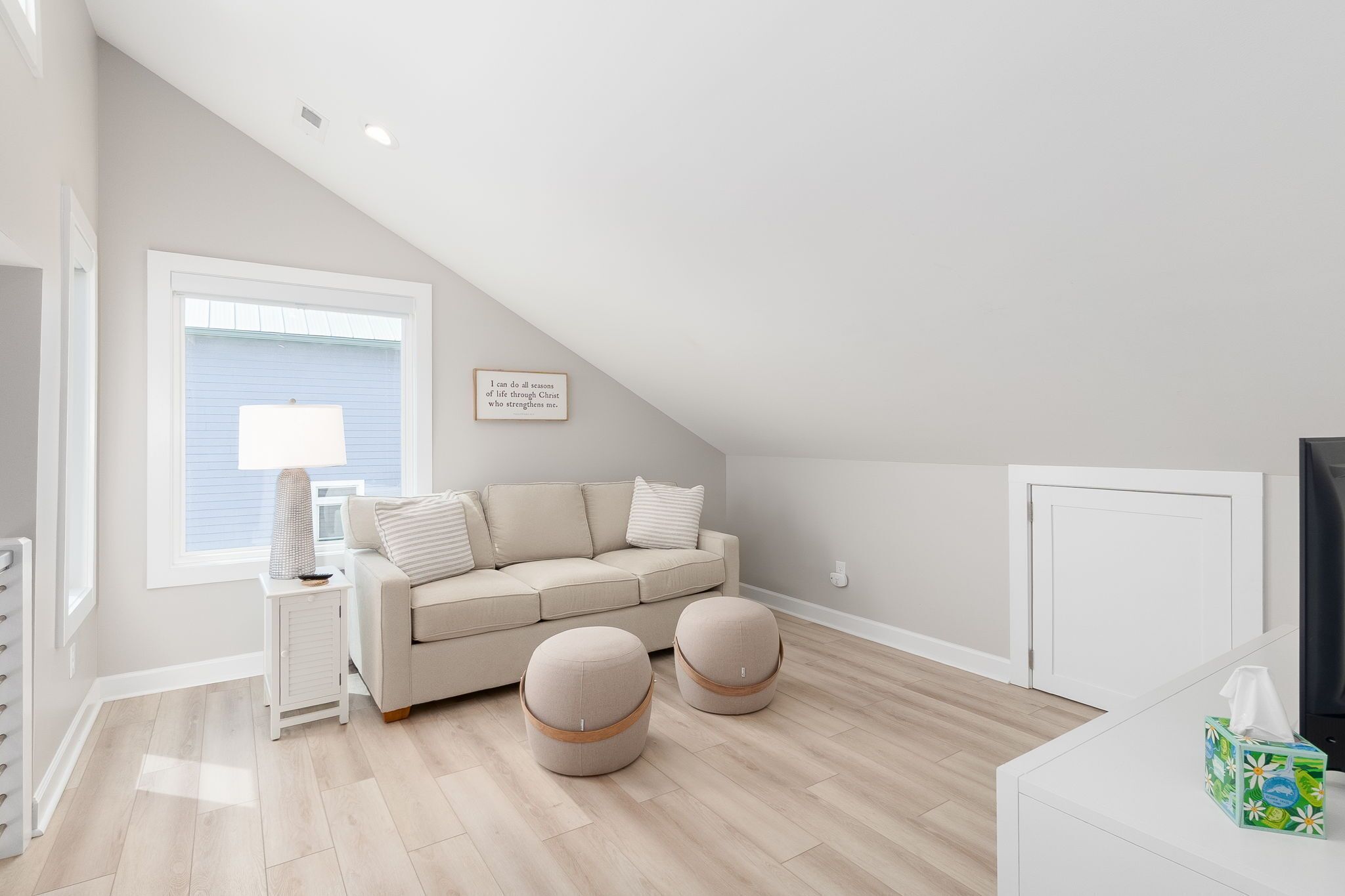 Et moderne, lyst værelse med en beige sofa, to skarmuer, et sofabord med lampe og et inspirerende citat i ramme på væggen.