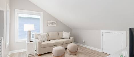 Et moderne, lyst værelse med en beige sofa, to skarmuer, et sofabord med lampe og et inspirerende citat i ramme på væggen.