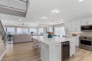 A modern kitchen with a central island, stainless steel appliances, and large windows offering a view. - Do Knot Disturb Oceanfront Private Pool Renovated Sleeps 14 (Emerald Isle)