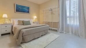 Ein Schlafzimmer mit einem Bett, Nachttischen, einem weißen Heizkörper, einem Gemälde und durchsichtigen Vorhängen.