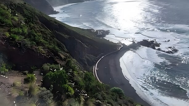 Eine Küstenlandschaft mit einer kurvenreichen Straße, steilen Klippen und einem Strand.
