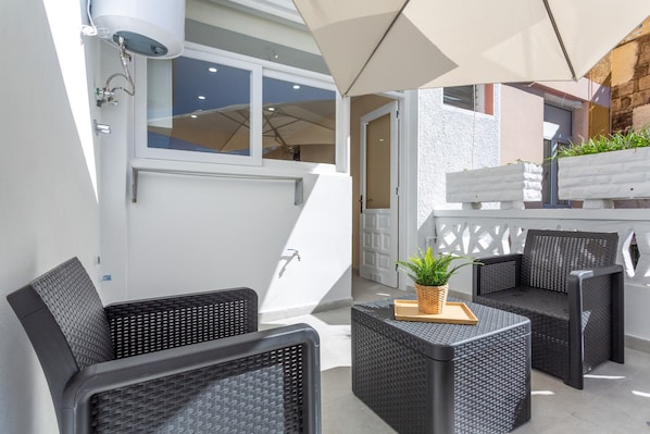 A modern outdoor seating area with wicker furniture, a potted plant, and a white wall with a window.