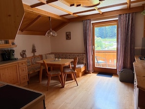 A cozy room with a wooden dining table, chairs, a bench, and a large window with curtains. - Cozy 4-person vacation apartment in the Pitztal, quiet and close to nature (Jerzens)