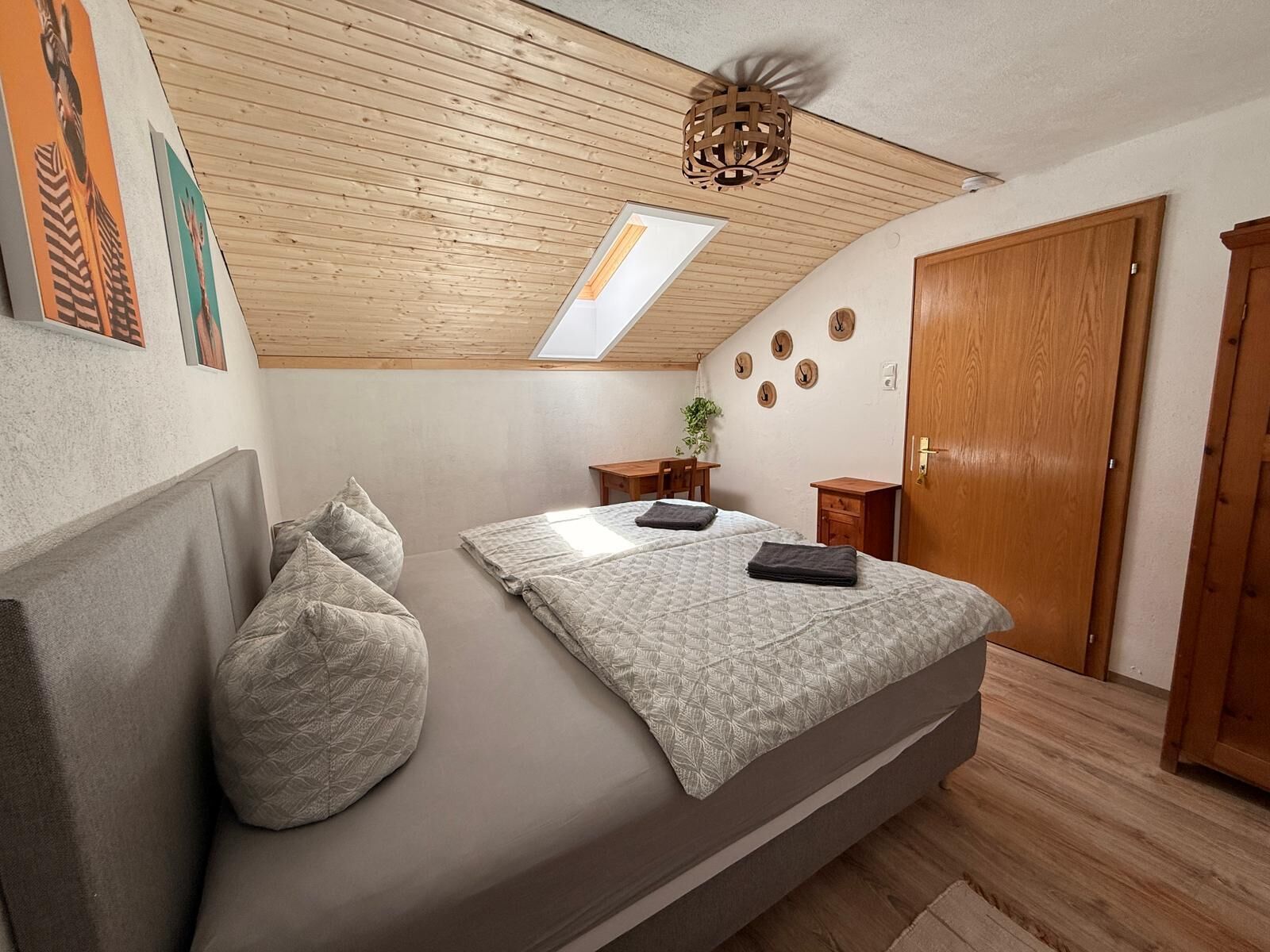 Une chambre avec un plafond en pente, un puits de lumière, un lit avec des oreillers, une petite table et une armoire.