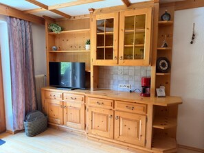 Une cuisine avec des meubles de rangement en bois, un téléviseur et une machine à café.