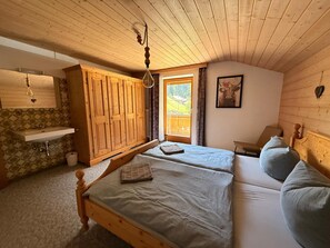 A room with a wooden ceiling, a bed with a white mattress, a wooden wardrobe, a small sink, and a window with a view of greenery. - Cozy vacation apartment for 4 people in the Pitztal Valley—quiet and close to nature (Jerzens)