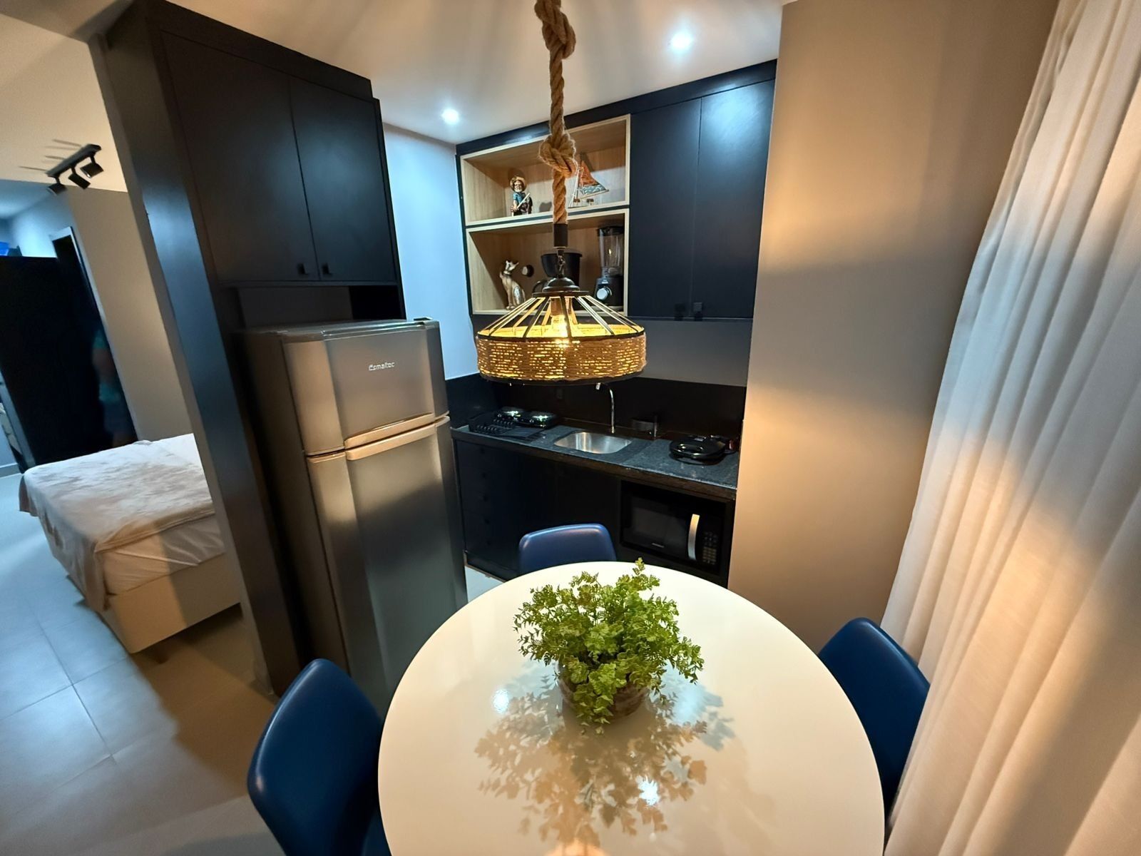 A modern kitchen with dark cabinets, a refrigerator, a sink, and a hanging light fixture.