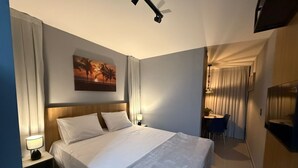 Habitación de hotel con cama, mesitas de noche, escritorio con silla, televisor y un cuadro en la pared.
