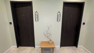 Un pasillo con dos puertas de madera oscura, una pequeña mesa de madera con un florero y un letrero con un número colgado en la pared.