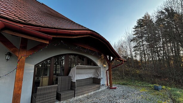 A covered outdoor seating area with wicker furniture, a stone-paved patio, and a red-tiled roof.