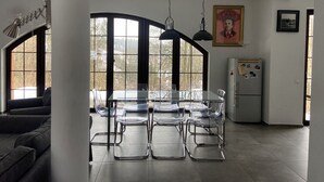 A modern kitchen with a dining table and chairs, large windows, and a refrigerator.