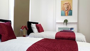 A hotel room with two beds, red and white bedding, a painting of a lion, and a plant on the dresser. - Prime Town Centre-Location-Station-Airport-WiFi-Parking (Luton)