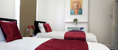 A hotel room with two beds, red and white bedding, a painting of a lion, and a plant on the dresser.
