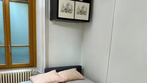 Ein Schlafzimmer mit einem Bett, einem Heizkörper, einem Fenster mit Jalousien und einem schwarzen Regal mit Dekoration.