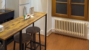 Eine moderne Küche mit Holztisch, zwei Barhocker, einer Deckenleuchte, einem Kühlschrank und einem Fenster mit Milchglas.