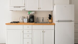 Une cuisine de taille réduite avec des meubles blancs, un évier en acier inoxydable, une machine à café et un réfrigérateur.