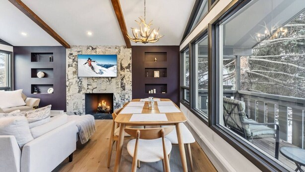 Een moderne woonkamer met een open haard, een eethoek en een groot raam met uitzicht op een besneeerd landschap.