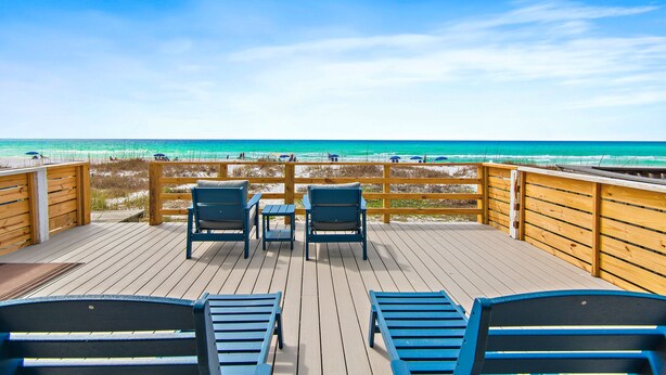 Une terrasse en bois, agrémentée de chaises et de tables, qui offre une vue sur la plage.