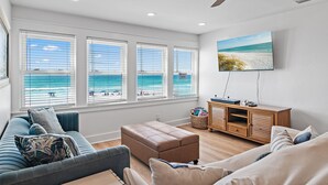 Un salon avec une grande fenêtre, un ventilateur de plafond, un téléviseur et un meuble en bois.