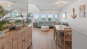 Un vaste espace de vie comprenant un canapé, une table à manger et des chaises, un meuble en bois et une grande fenêtre équipée de stores.