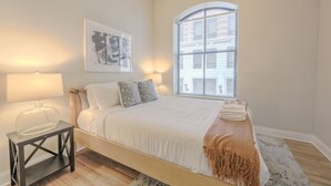 Ein Schlafzimmer mit Bett, Nachttischen, einem Fenster mit Jalousien und einem Wandbild.